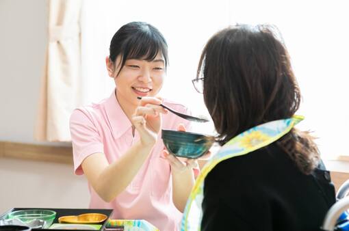職員が入居者に食事の介助をしている様子。温かみのある食事場面。
